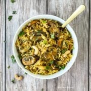 A white bowl is with mushroom rice and topped with cilantro and cashews