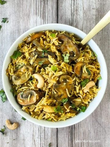 A white bowl is with mushroom rice and topped with cilantro and cashews