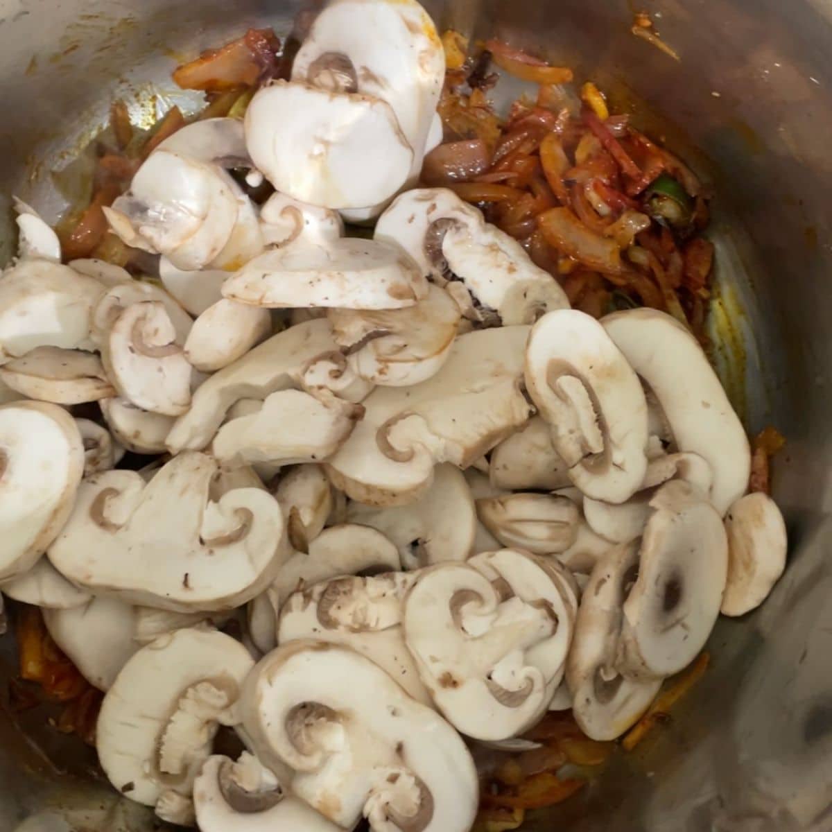 A pot is with spices, onions and sliced mushroom over the heat.