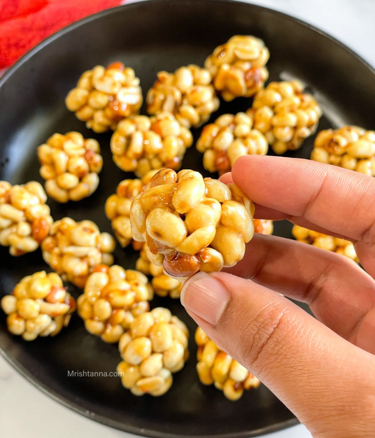 A peanut jaggery ladoo is held in a hand.