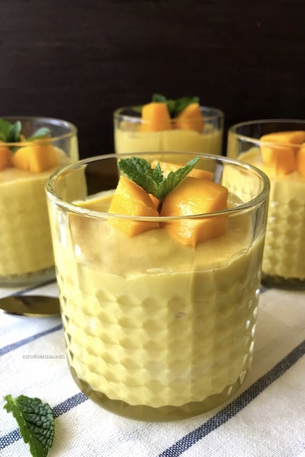 A glass of mango mousse and topped with cubed fresh mangoes