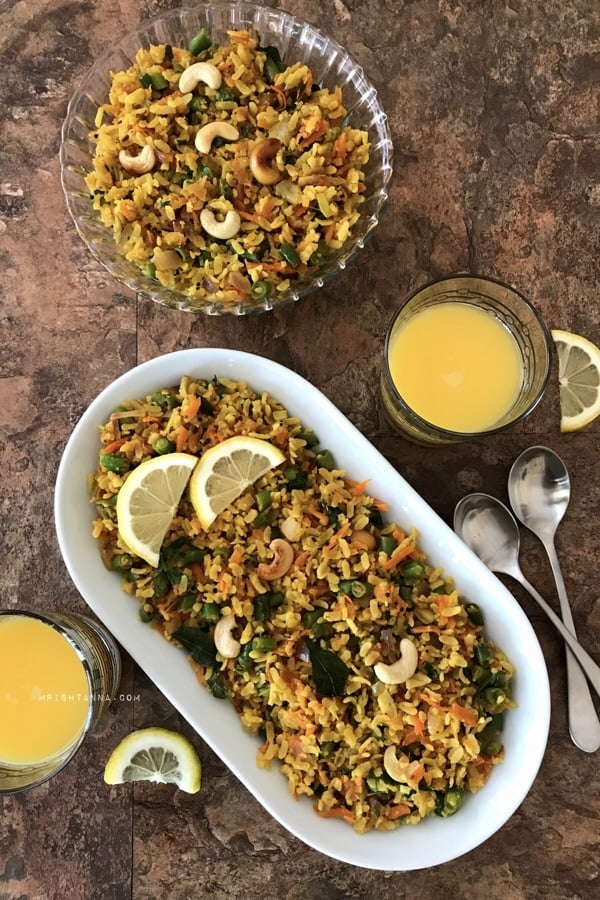 A bowl of vegetable poha is on the table with a cup of orange juice