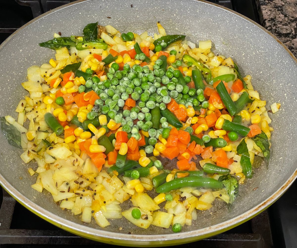 A pan is with mixed vegetables and spices over the heat.