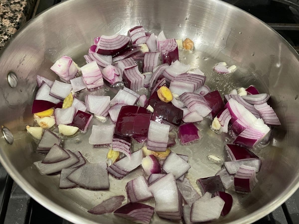 A pan is with onions, garlic and tomatoes over the heat.