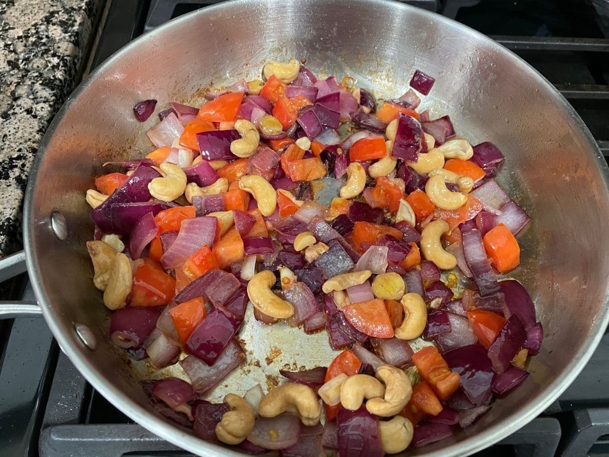 A pan is with vegetables and cashews over the heat