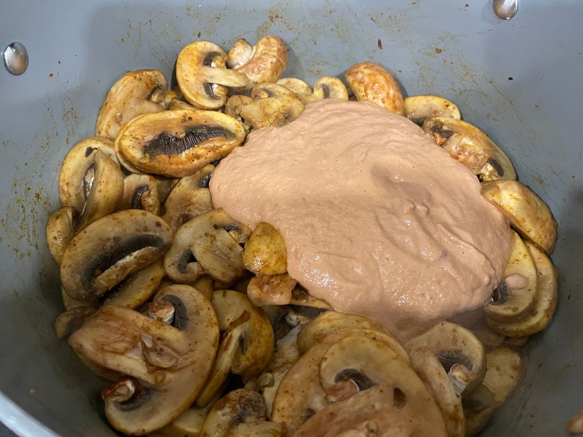 A pan is with tomato puree and mushrooms over the heat
