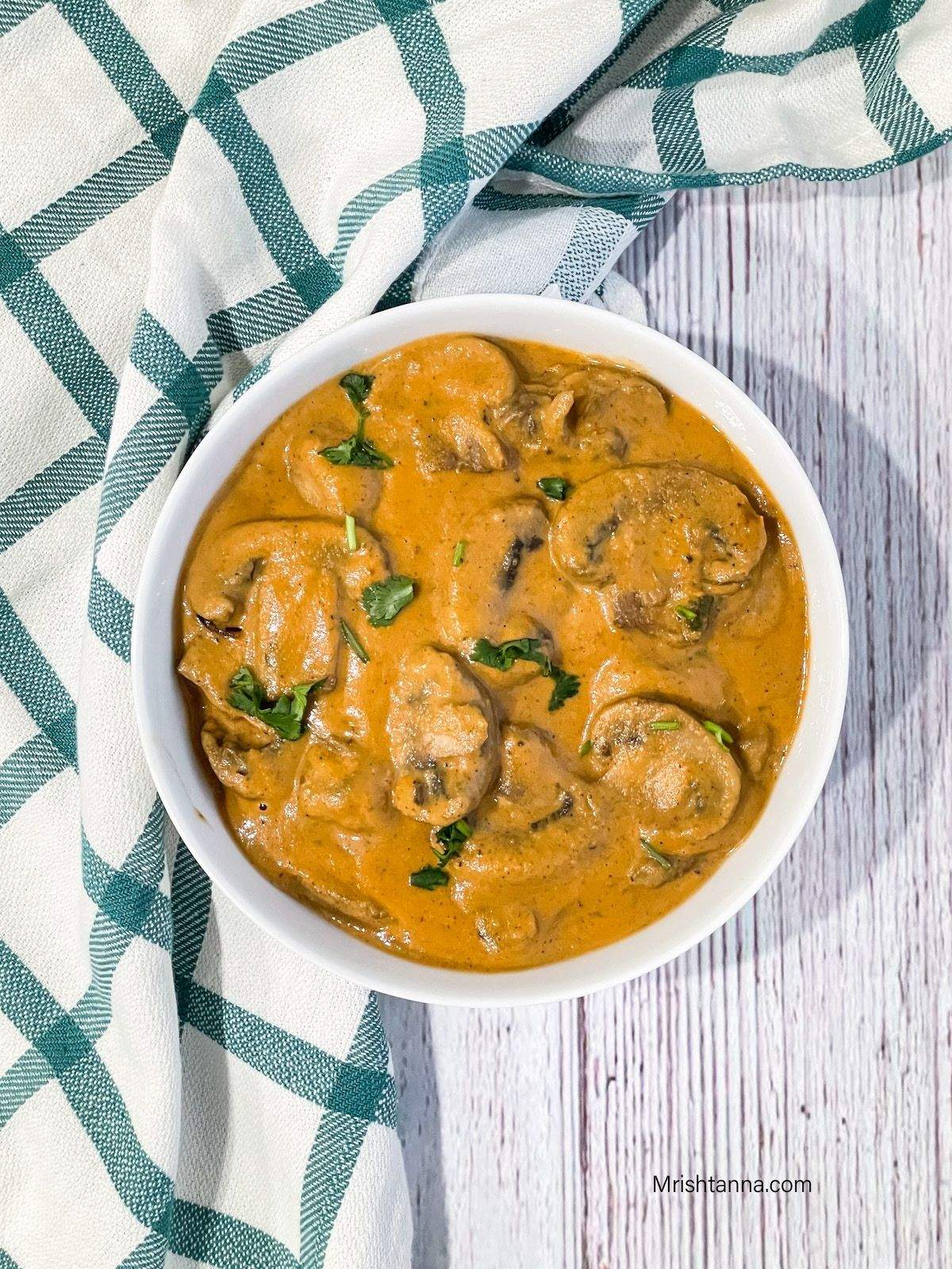 A bowl is filled with mushroom masala and topped with cilantro.