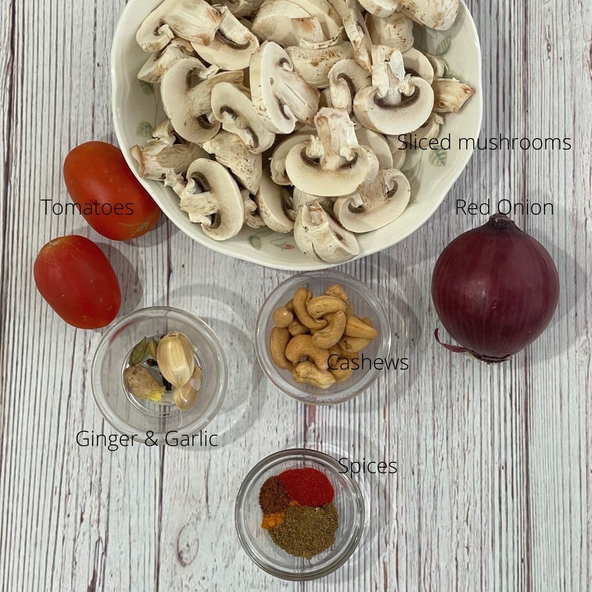 Ingredients for mushroom masala is on the table like onion, tomato, mushrooms and spices.