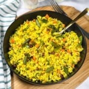 A plate of vegetable poha is on the wooden board and a spoon is inserted.