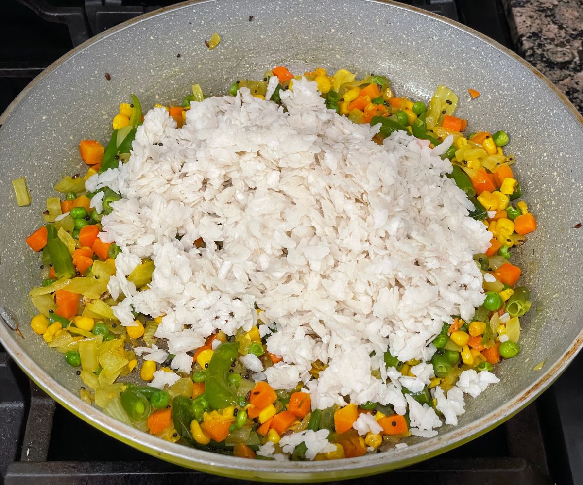 A pan is with poha and mixed vegetables over the heat.