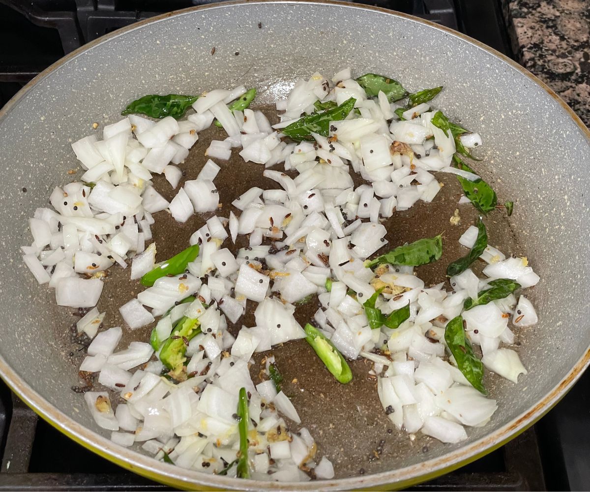 A pan is with oil, spices and chopped onions over the heat.