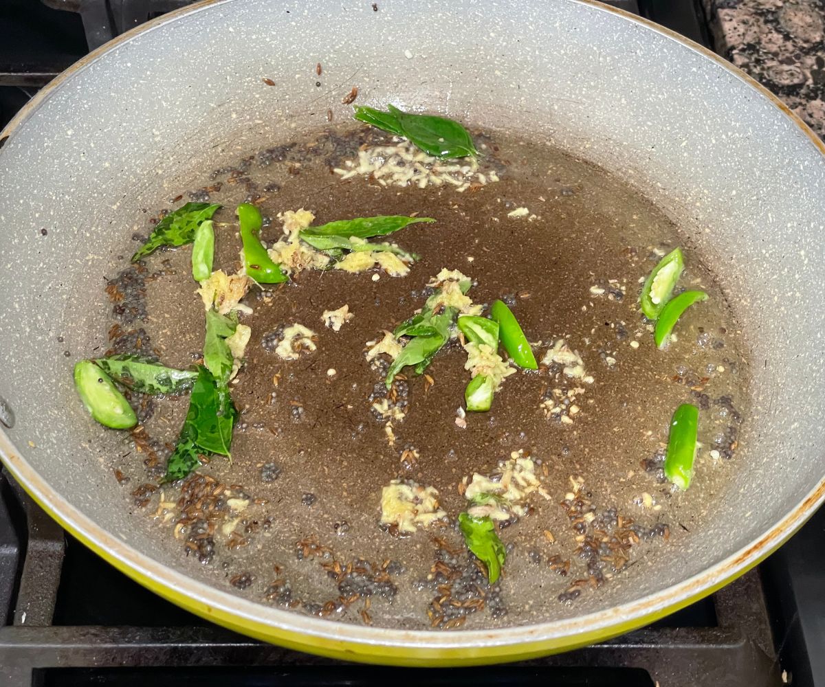 A pan is with oil, spices and green chilies over the heat.