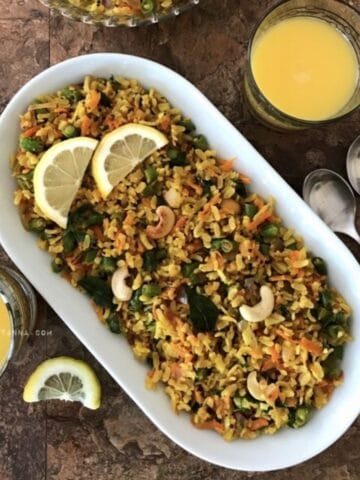 A plate of vegetable poha is on the table and topped with lemon slices