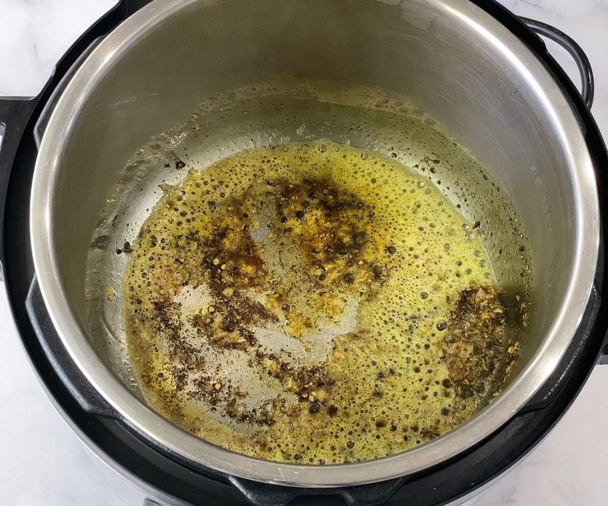 An instant pot is with ghee, spices and ginger on saute mode.