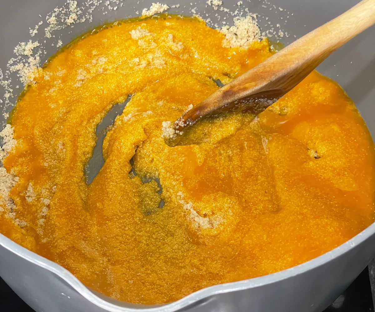 A pan is with roasted rava and mango pulp over the flame.