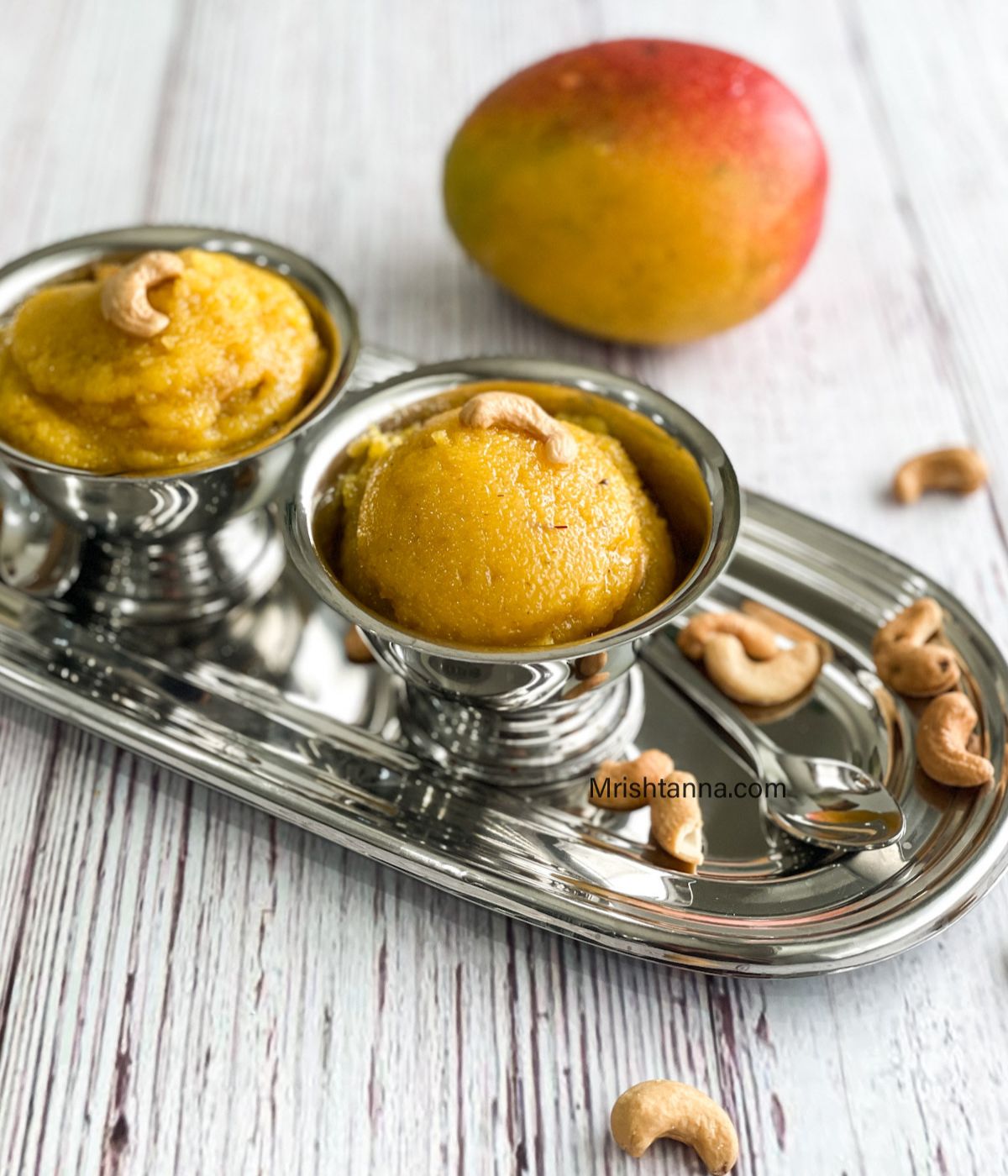 A steel cups are with mango halwa on the tray.