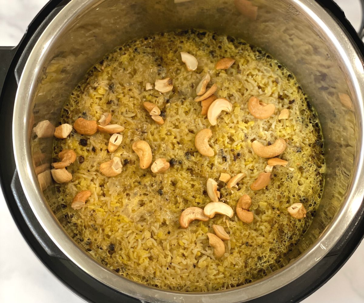 An instant pot is with ven pongal and topped with roasted cashews.