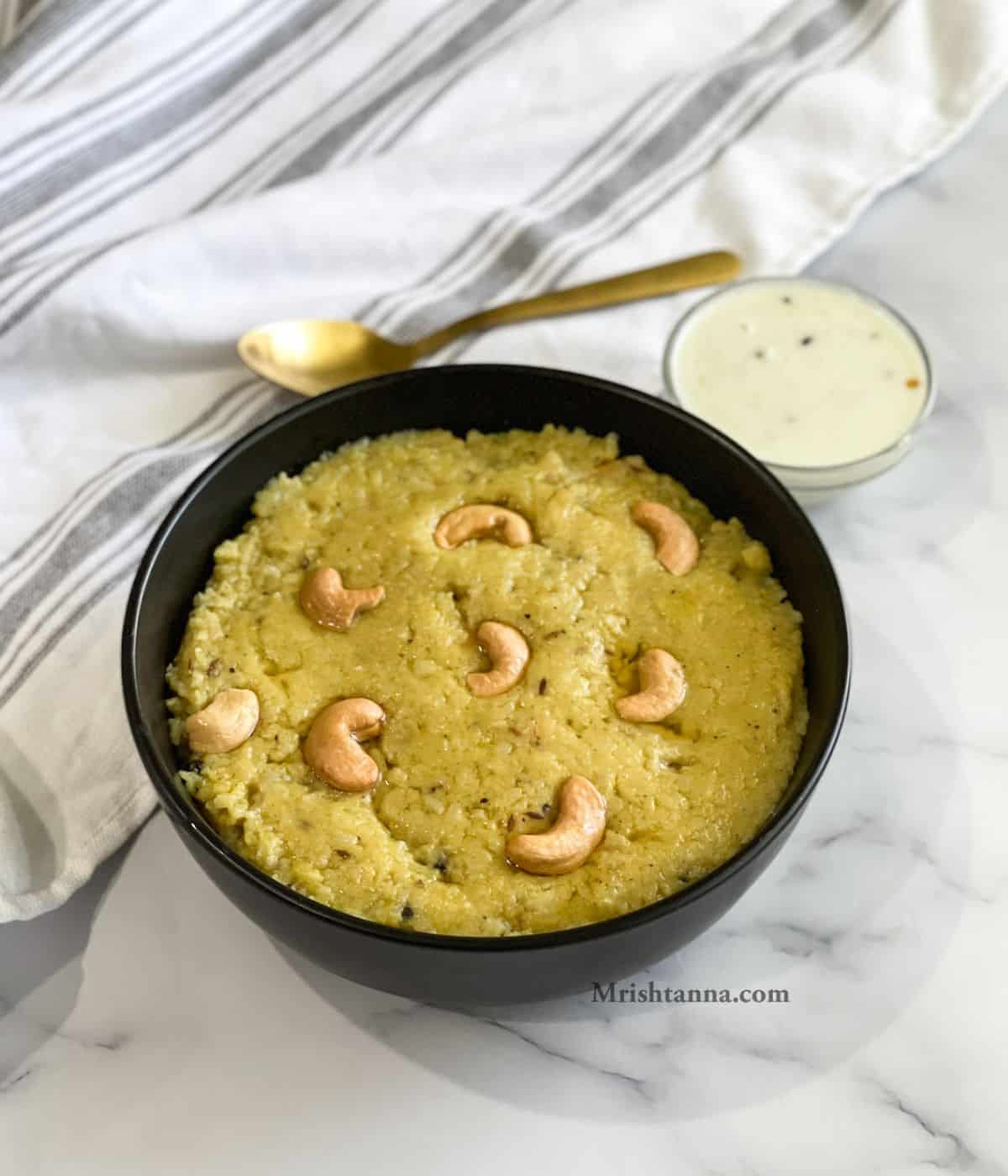 A bowl is with ven pongal and chutney on the table.