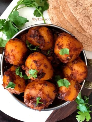 A bowl with masala potatoes and topped with cilantro and placed on the white serving tray