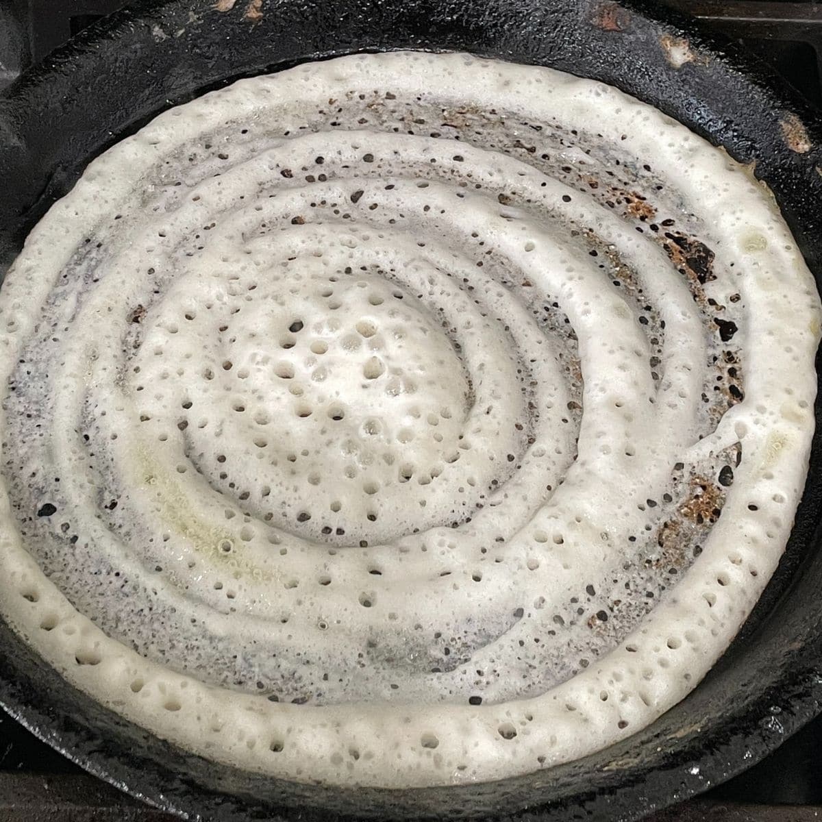 A cast iron pan is with dosa over the heat