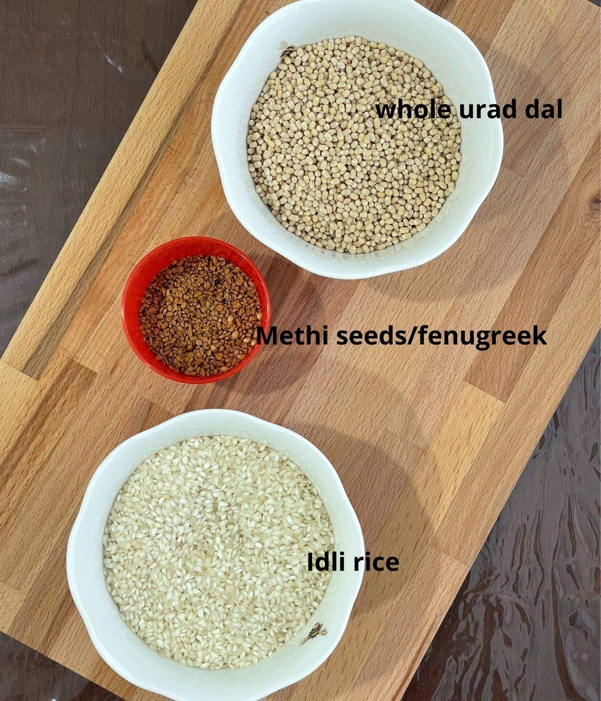 A board is filled with bowls of urad dal,rice and methi seeds