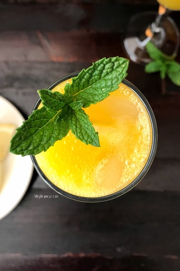 A glass of mango mocktail is on the table and topped with mint leaves.