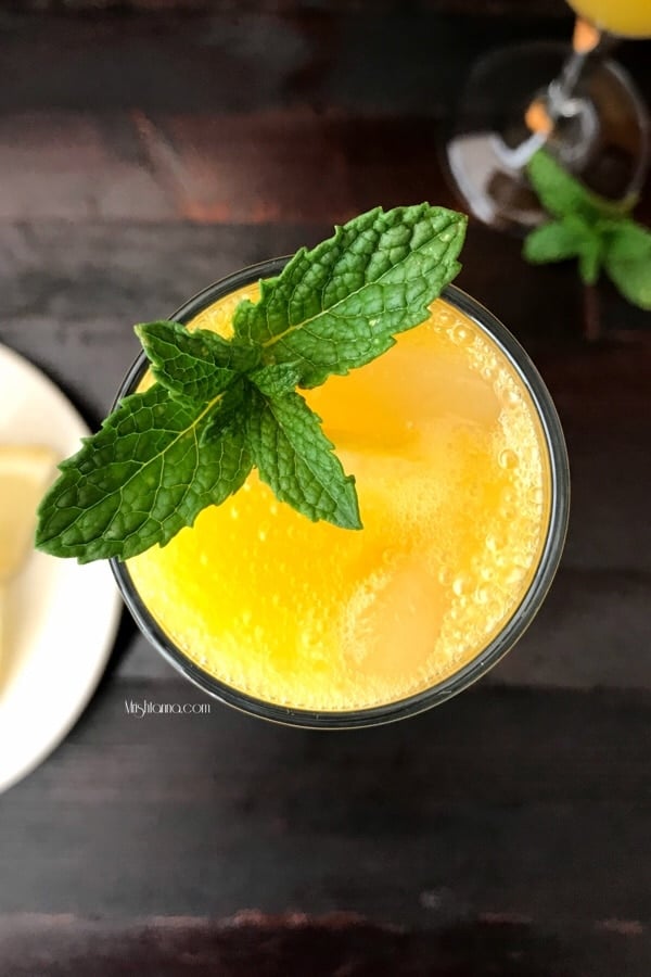 A glass of mango mocktail is on the table and topped with mint leaves.