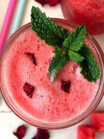 A glass is filled with watermelon juice and topped with mint leaves.