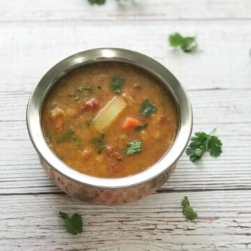 A pot is with sambar and topped with cilantro on the table