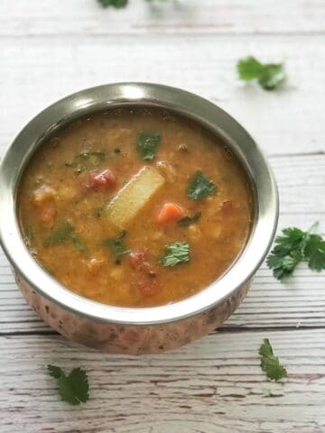 A pot is with sambar and topped with cilantro on the table