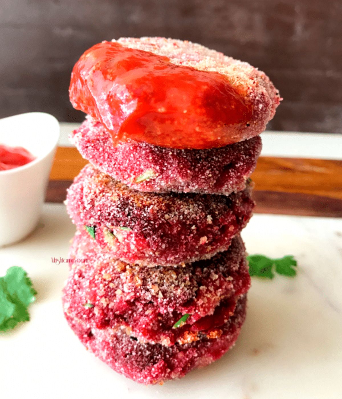 Four beetroot cutlets are stacked and dipped in to tomato ketchup.