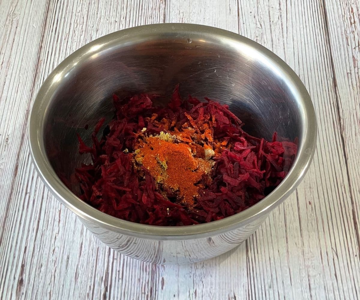 A bowl is with grated beets and spices on the table.