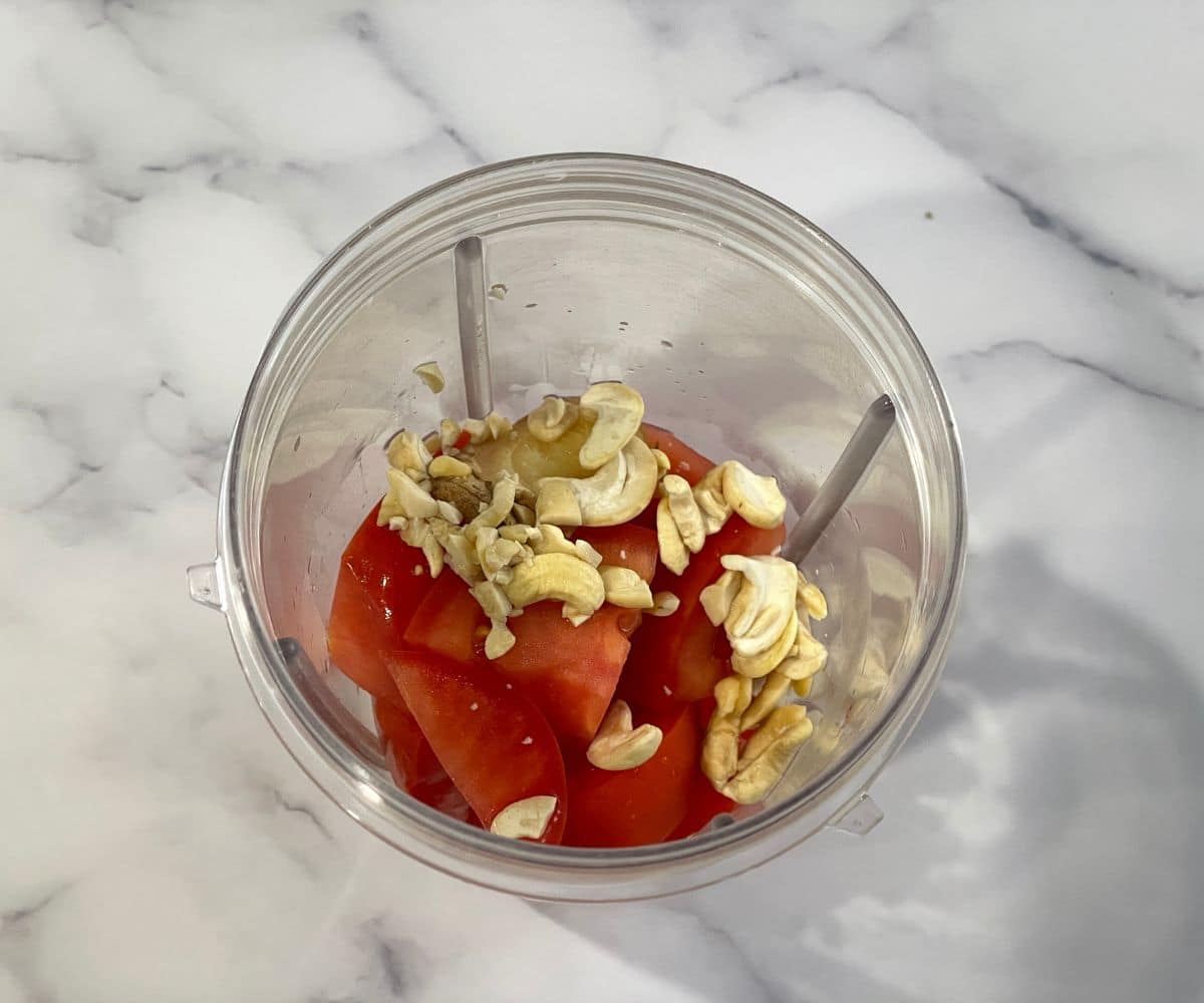 A blender is filled with tomatoes, tofu, cashews.