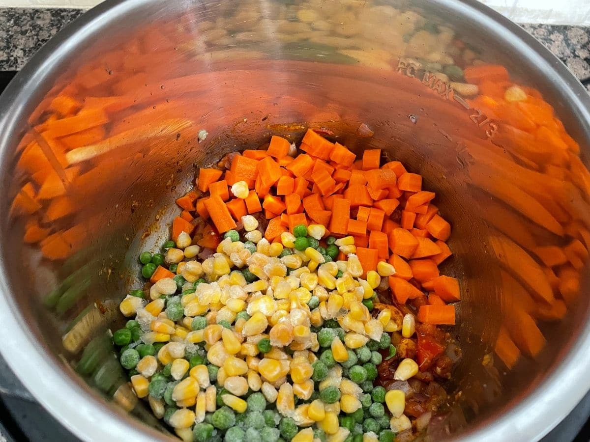 An instant pot is filled with peas, corn and chopped carrots