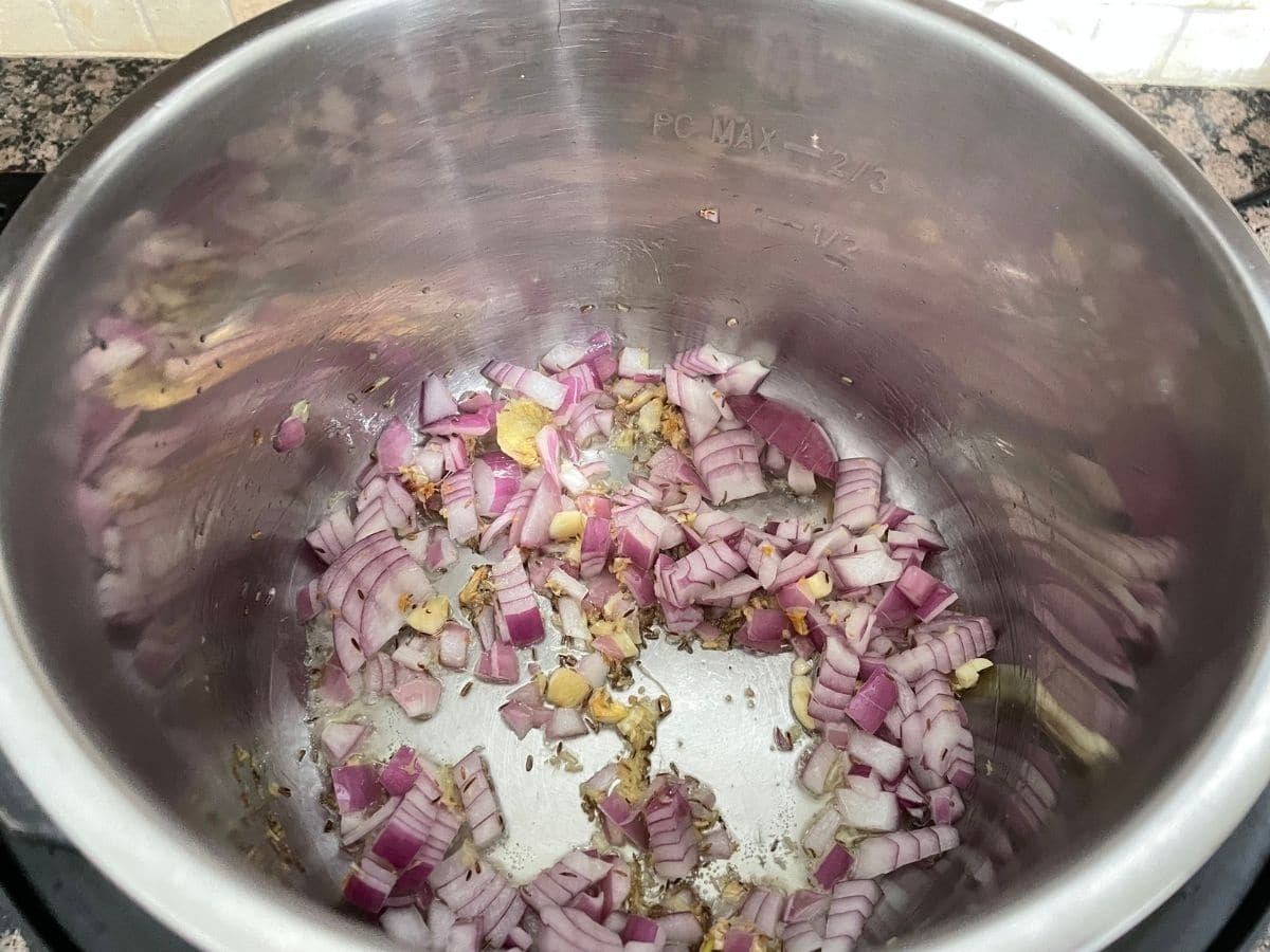 An instant pot is with spices, onions, and garlic with heat on.