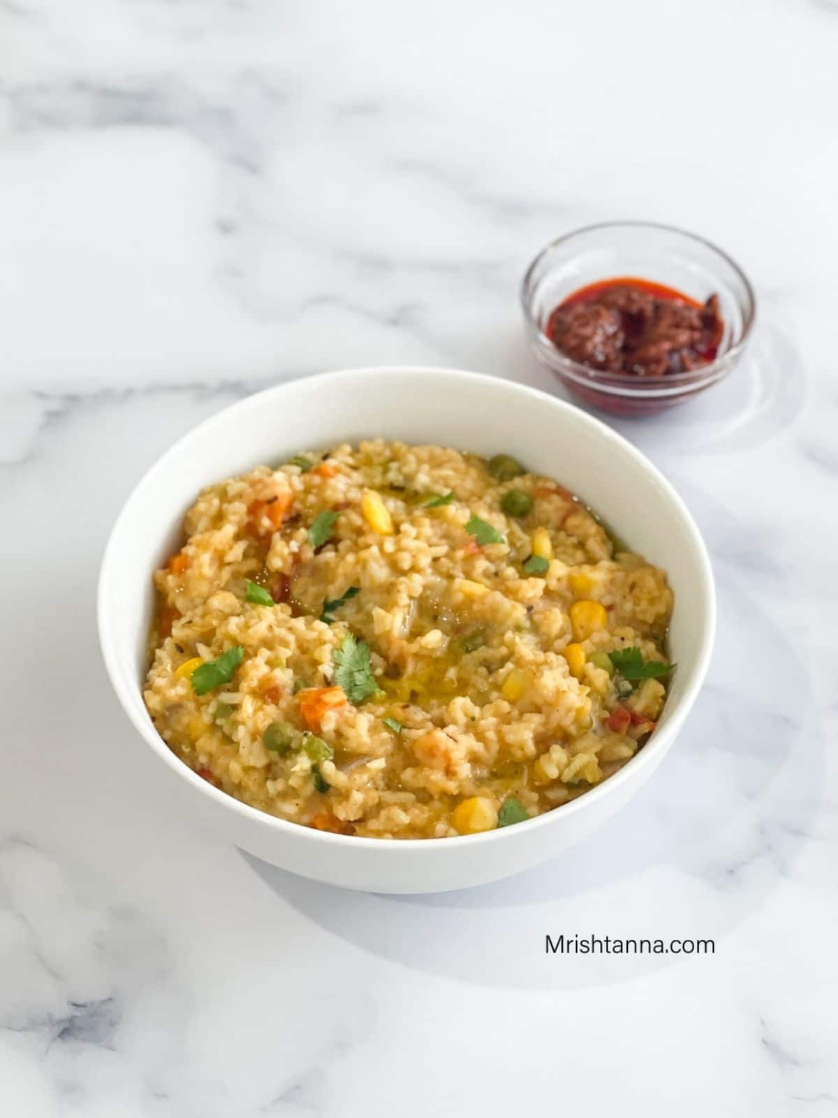 A bowl of masala khichdi is on the table along with tomato pickle