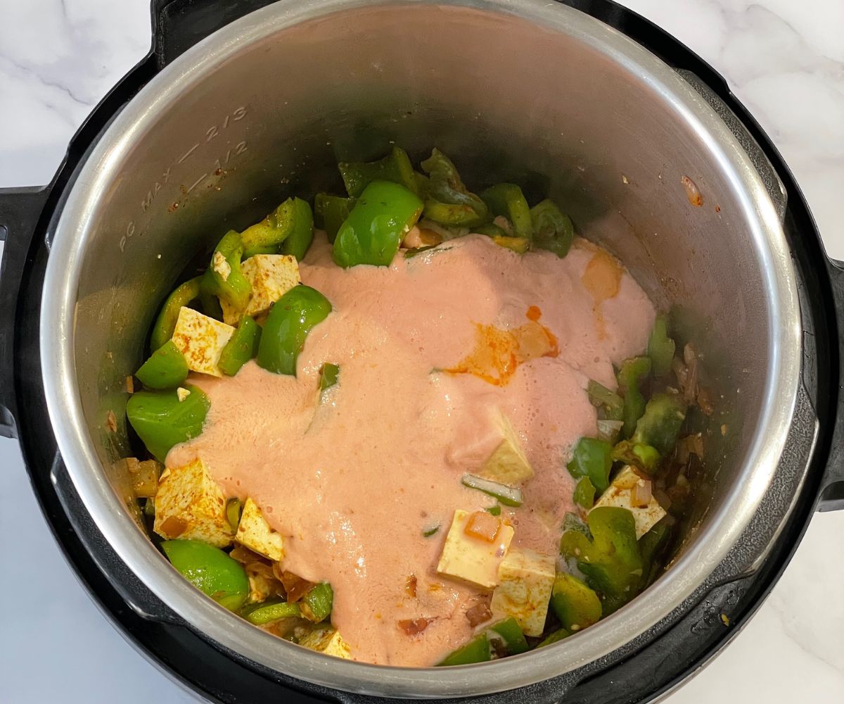 An instant pot is with bell peppers, tofu and tomato puree for curry.