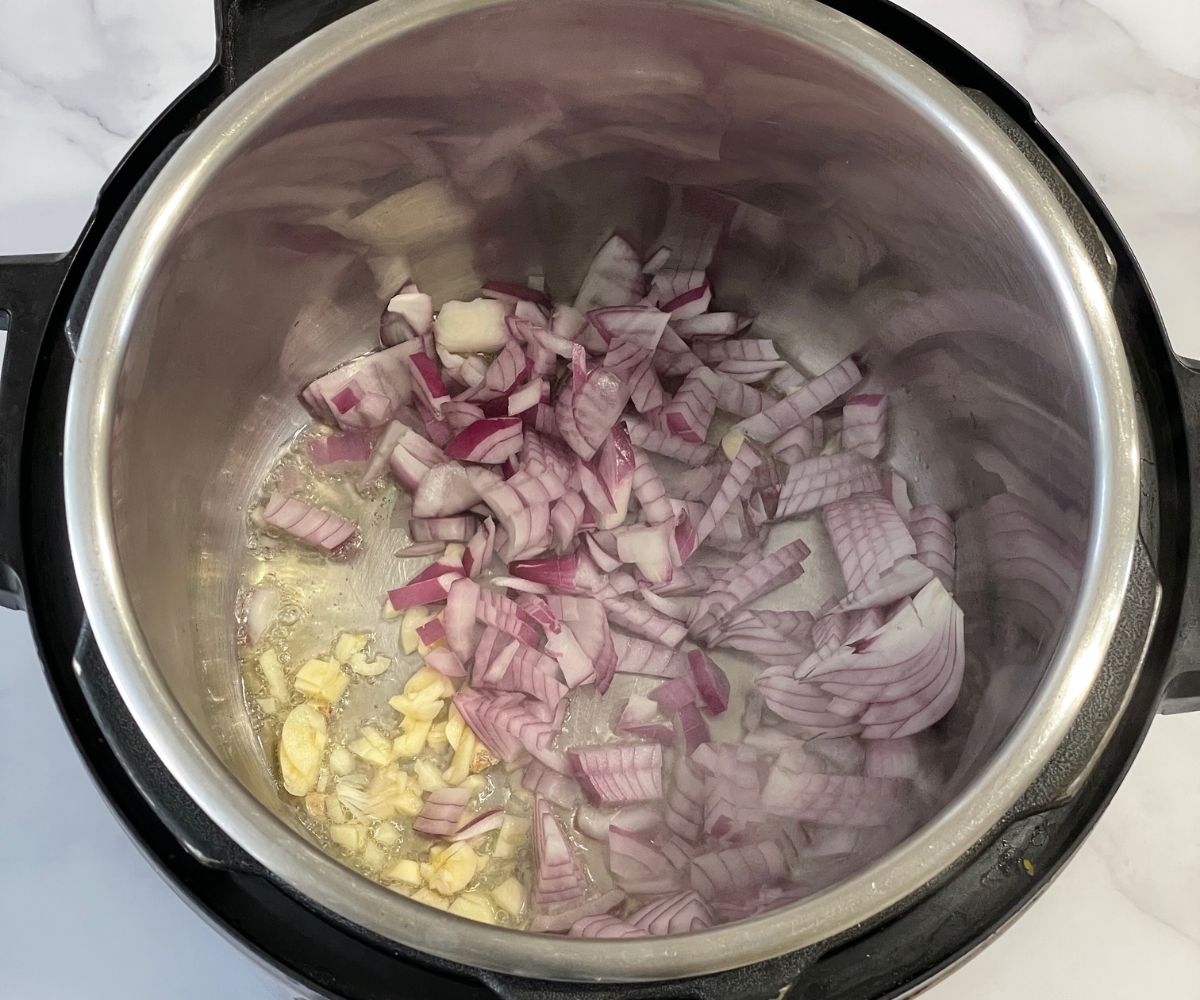 An instant pot is with onions and garlic on saute mode.
