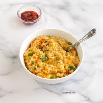 A bowl of instant pot khichdi is on the table with spoon inserted.