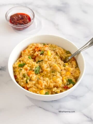 A bowl of instant pot khichdi is on the table with spoon inserted.