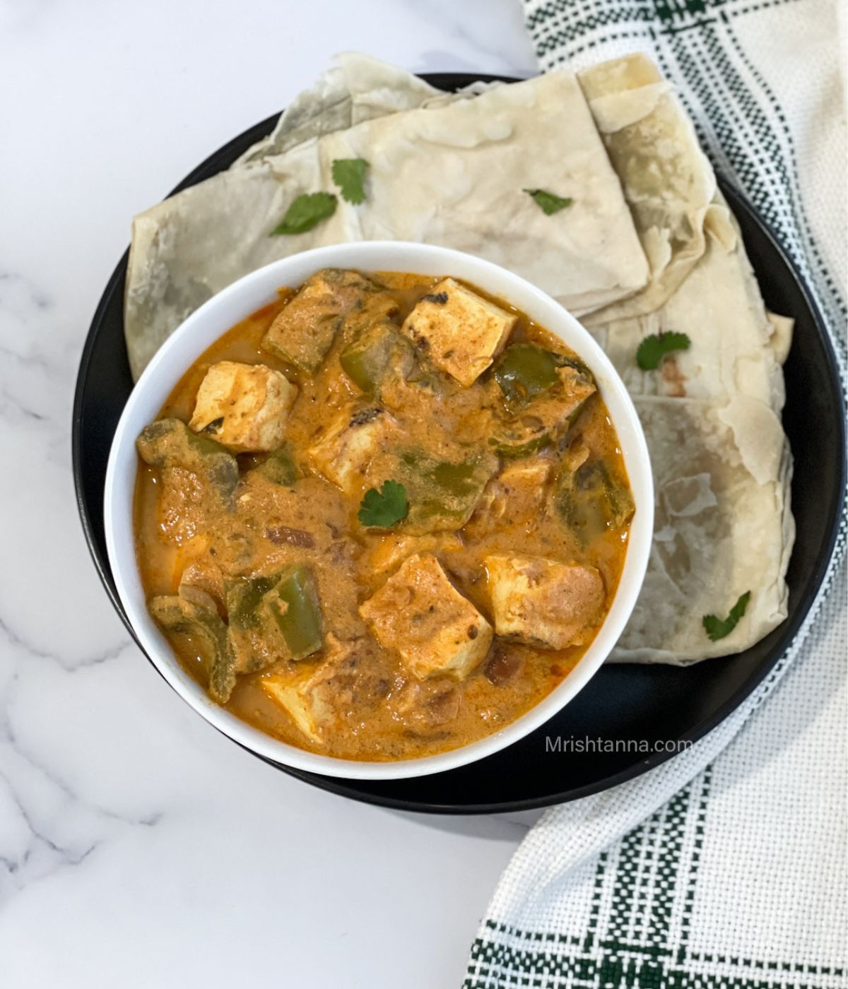 A bowl of tofu curry is on the plate with rotis.