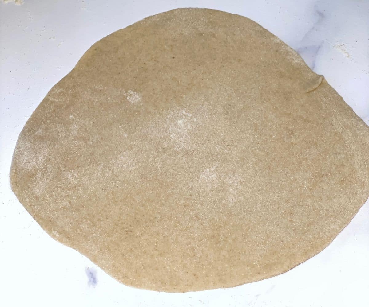 A flour is covered with rolled naan dough.
