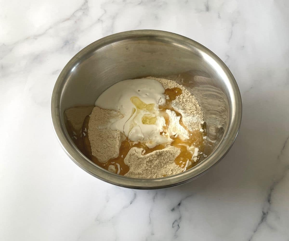 A bowl is with flour, salt and vegan curd to make naan recipe.