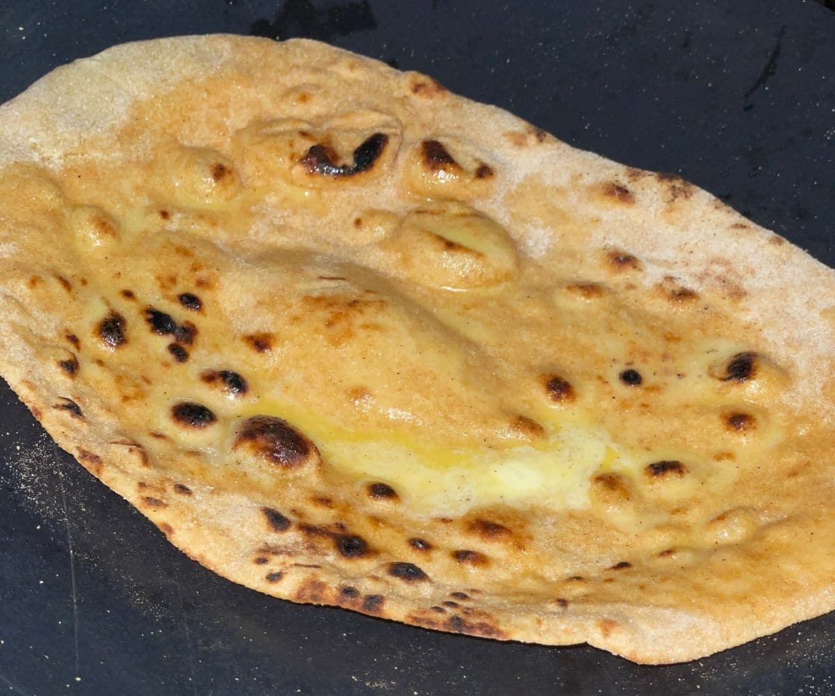 A wheat naan is on the hot tawa and topped with vegan butter.