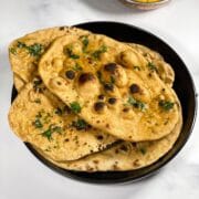 A plate of whole wheat naan is on the table along with curry.