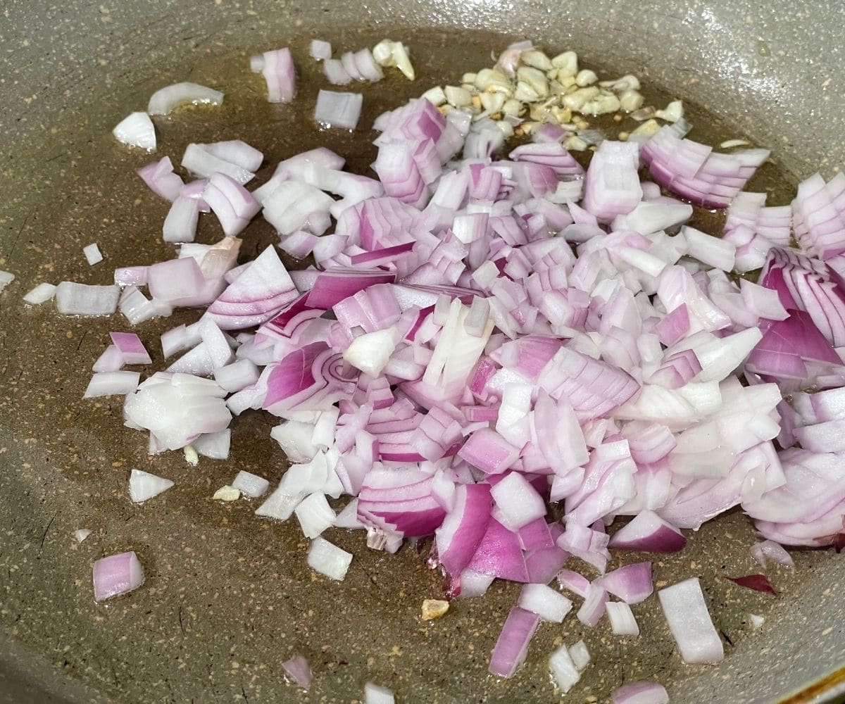 A pan is with onions and garlic over the flame.
