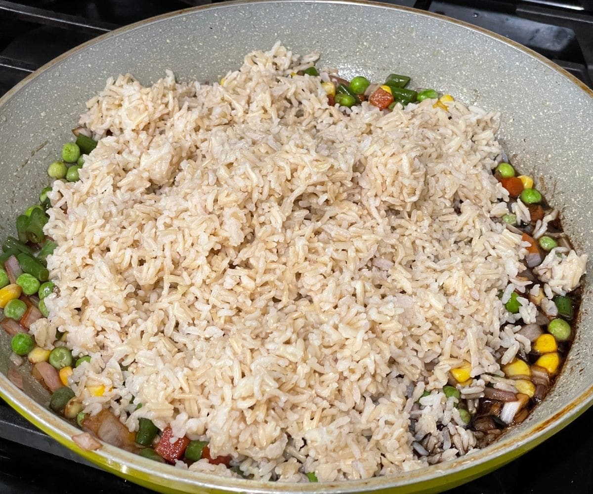 A pan is filled with brown rice and sauces over the heat.
