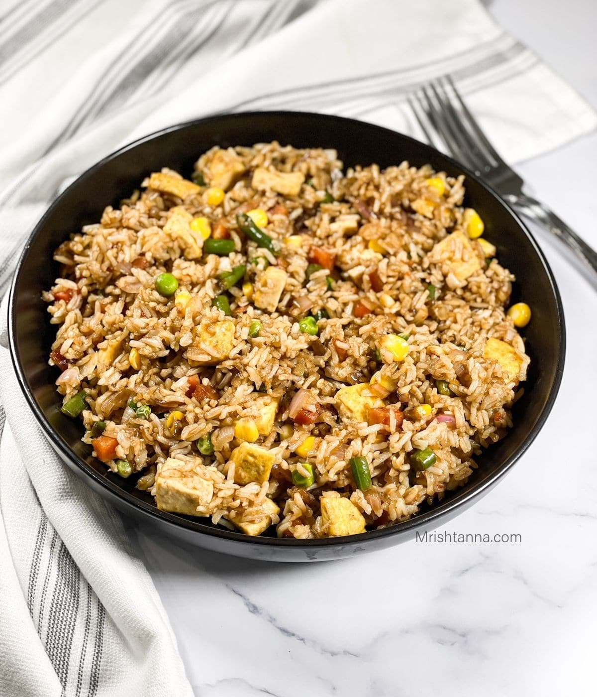 A black plate is with vegan fried rice with tofu.