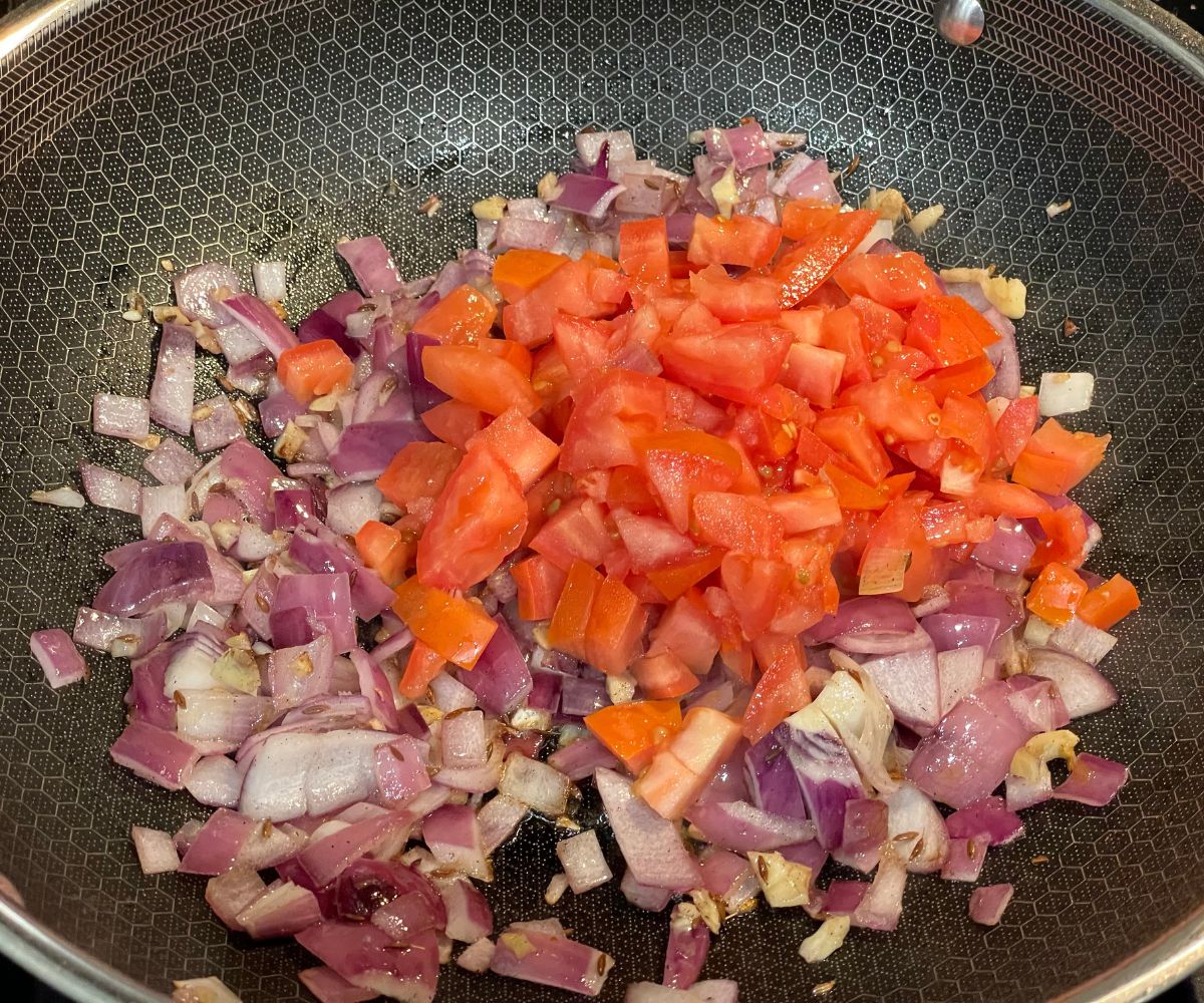A pan is with onions and tomatoes.