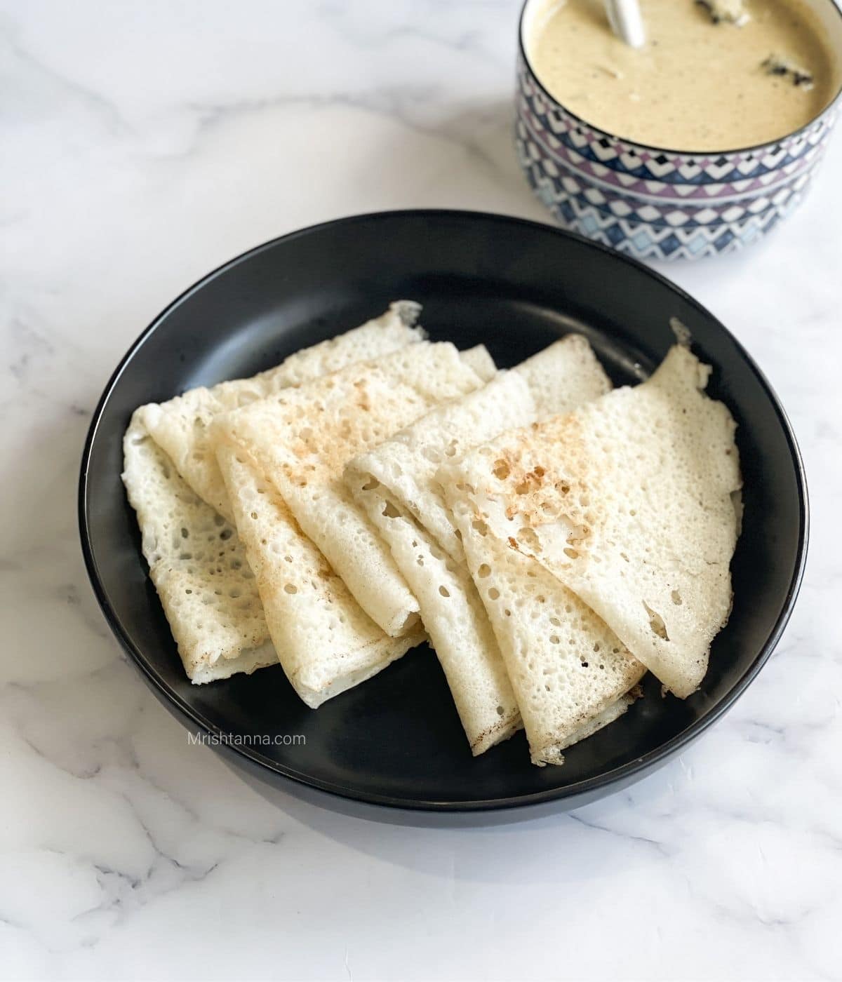 A plate has folded neer dosa and bowl of chutney by side.